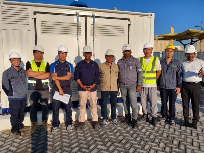 Workers pose before an industrial equipment container